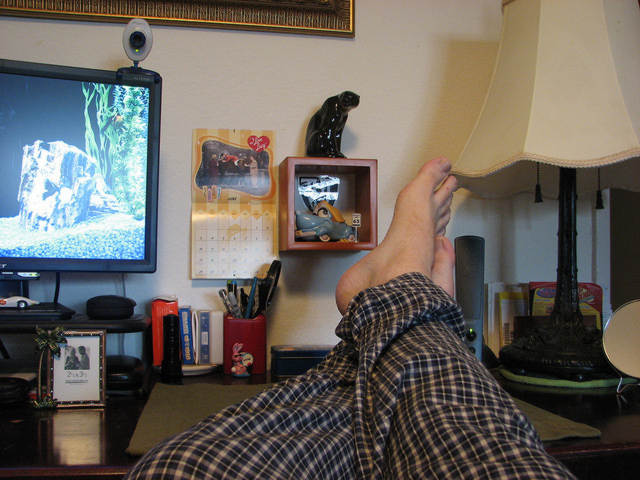 feet on a desk with tv computer webcam home office study working from home pajama pants 